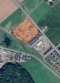 Large residential property in development with surrounding roads, nearby fields, industrial buildings, residential areas, trees, and water bodies