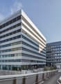 Modern office building with glass facade, multiple floors, and a landscaped area in front.