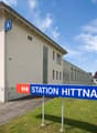 A building with a sign that reads 'Station Hittnau', a large window, and a red carpet leading to the entrance.