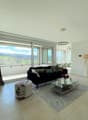 Spacious living room with large windows offering a scenic view, black sofa, glass coffee table, area rug, and decorative lamps