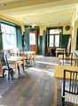 Wooden floor, rectangular dining tables, wooden chairs with striped cushions, green walls, wooden door, large windows, ceiling lamps