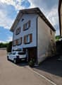 2-story house with gray exterior walls, brown wooden shutters, and a parked car in the driveway.