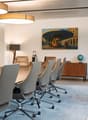 spacious room, white walls, large wooden table, multiple modern chairs, lamp, wooden desk, painting, whiteboard, rug