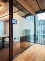 An empty conference room with glass walls, a table, chairs, and a monitor on the wall.