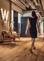 Large room with modern lighting, wooden floor, decorative pillows, a woman walking, brown leather armchairs, a 'W' light sign on the wall