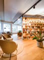 large wooden bookshelves, wicker chairs, round rug, desk, green plants, wooden counter, glass walls, windows