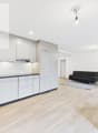 modern kitchen with white cabinets, wooden floor, black countertop, sink, faucet, black couch, rug, wooden table, chairs, potted plant