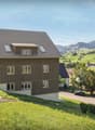 Modern house, brown exterior, large windows, located on a hill, surrounded by green fields and mountains