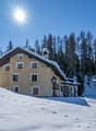 2-story house, beige exterior, covered in snow, balconies, pine trees in the background