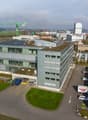 Office building, 4 stories, large windows, grey and white exterior, solar panels on the roof, parking area with cars