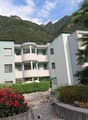 Modern apartment building, multiple floors, balconies, surrounded by greenery, mountain view
