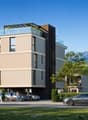 Modern multi-story building with a glass-enclosed terrace on the top floor, surrounded by greenery and mountains in the background.