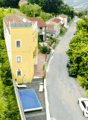 Building with yellow walls, swimming pool, red roofs, surrounded by houses and vegetation