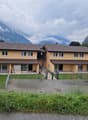 2 story house, yellow exterior, brown roof, large windows, fenced yard, mountains in the background