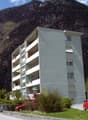 white apartment building, several balconies, mountain landscape, red cars parked
