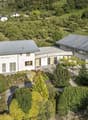 Large villa with several sections, gray roof, surrounded by greenery, visible from a distance