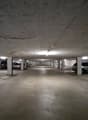 concrete floor, white ceiling, rows of parking spots, lights on the ceiling, metal columns, some cars parked
