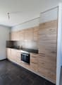 Modern and minimalistic kitchen with wooden cabinets, black countertops, built-in oven and sink with faucet, light fixtures