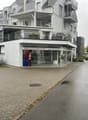 An apartment building with several floors and a storefront at the ground floor, with a car parked in front of it.