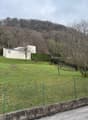 A sloping garden with trees and bushes, fenced on one side, and overlooking the hills.
