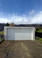 Garage with a white door, concrete walls, gravel driveway, fenced area, green field, mountains in the background
