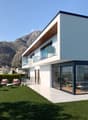 Modern white villa with large windows, patio with outdoor furniture, terrace, and mountain view.