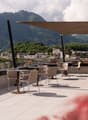 A terrace with a canopy, chairs, tables, surrounded by plants, views of the mountains
