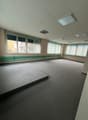 An empty room with gray carpet floor, white ceiling, large windows with metal blinds, and an elevated platform on the left.