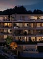 modern apartment building, multiple floors, balconies, outdoor seating areas, garden, illuminated at night