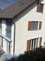 2 story house, white exterior, brown roof, brown shutters, large windows, patio with table and chairs