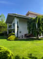 modern house with 2 floors, red tiled roof, large balcony on 2nd floor, garden with lawn and trees, outdoor dining area