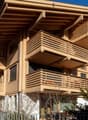 Modern wooden apartment building with multiple balconies, large windows, and a sloped roof