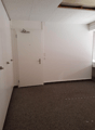Small, rectangular room with two white doors, empty carpet floor, and white walls with visible lighting switches.