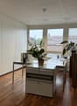 An empty office with white walls, wooden floor, white cabinets, two desks, and two potted plants.