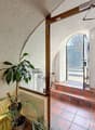 open door, arched window, red tiled floor, plants, wooden cabinet, open door leading to outside