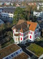 Two story house with brown roof, red windows, balcony, small garden