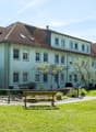 2 story house, white walls, brown roof, multiple windows, stairs, balcony, garden, benches