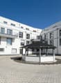 Modern white building, multiple windows, balconies, brick driveway, gazebo, car parked