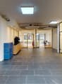 Open space office with glass walls, wooden floors, white walls, modern furniture, and ceiling lights.