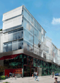 Modern building with glass facade, red awning, green roof, multiple floors, urban setting