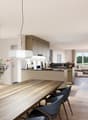 Dining room with wooden table, chairs, flowers in a vase, kitchen with island, open to living room, modern design, white walls, wooden floors, large windows