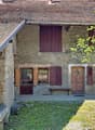 Stone house, brown roof, wooden doors, wooden shutters, wooden bench, stone wall, grassy area