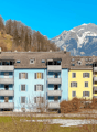 multi-story residential building, balconies on each floor, snow on ground, mountainous background