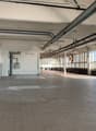 Large open commercial space with high ceilings, exposed ductwork, and tiled flooring. The space appears to be a warehouse or industrial facility with multiple windows along one side providing natural light. There are no visible furnishings or equipment, s