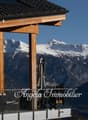 Wooden chalet-style building with a balcony overlooking snow-capped mountains in the background. The building has the name 'Angela Immobilier' displayed on the front.