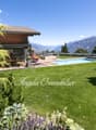 Luxury house with wooden exterior, surrounded by lush greenery and mountains in the background. The property features a swimming pool and offers a scenic view of the surrounding landscape.