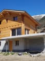 New construction house made of wood and concrete, surrounded by nature with mountains in the background, balcony, garage