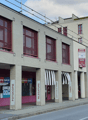 Two-story building, brick construction, red shutters, signage for various shops, multiple entrances