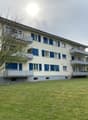 3 story apartment building, white walls, blue shutters, balconies, large grassy area