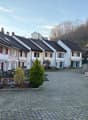 Row of houses, white walls, black roofs, red shutters, brick driveway, small garden in front, trees in the background